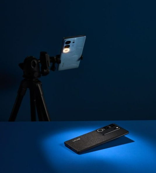 Ein Smartphone auf einem Stativ, ein weiteres auf blauer Oberfläche. Blauer Hintergrund.